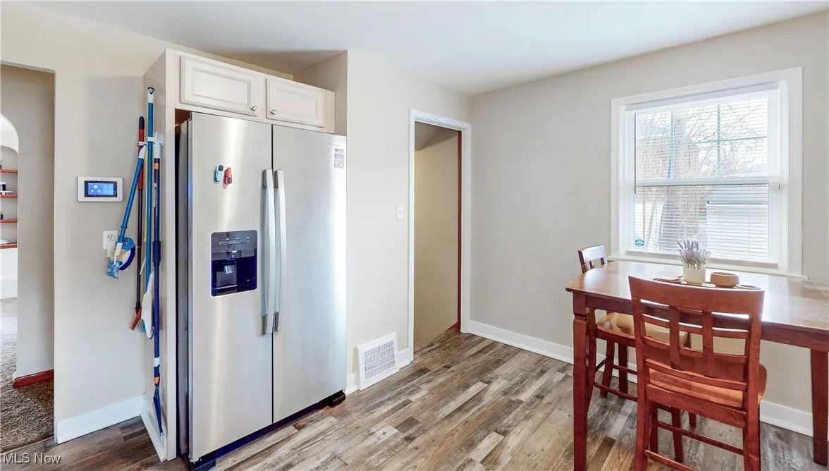 Kitchen with light wood-style floors, stainless steel fridge with ice dispenser, baseboards, white cabinetry, and visible vents