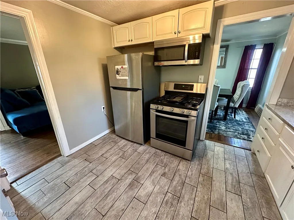 Kitchen featuring a textured ceiling, crown molding, white cabinets, appliances with stainless steel finishes, and light wood-type flooring
