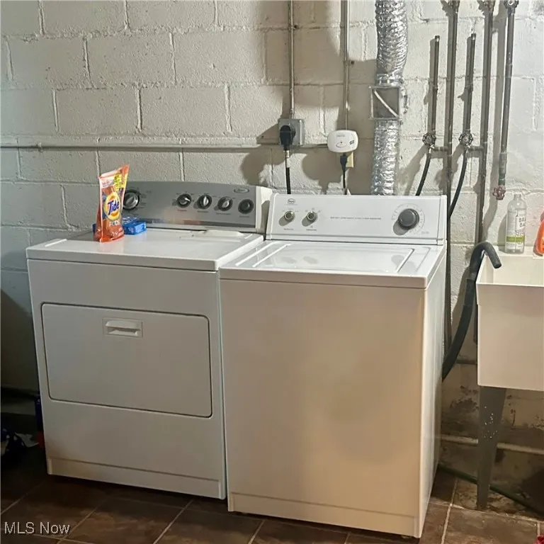 Washroom with separate washer and dryer, concrete block wall, and a sink
