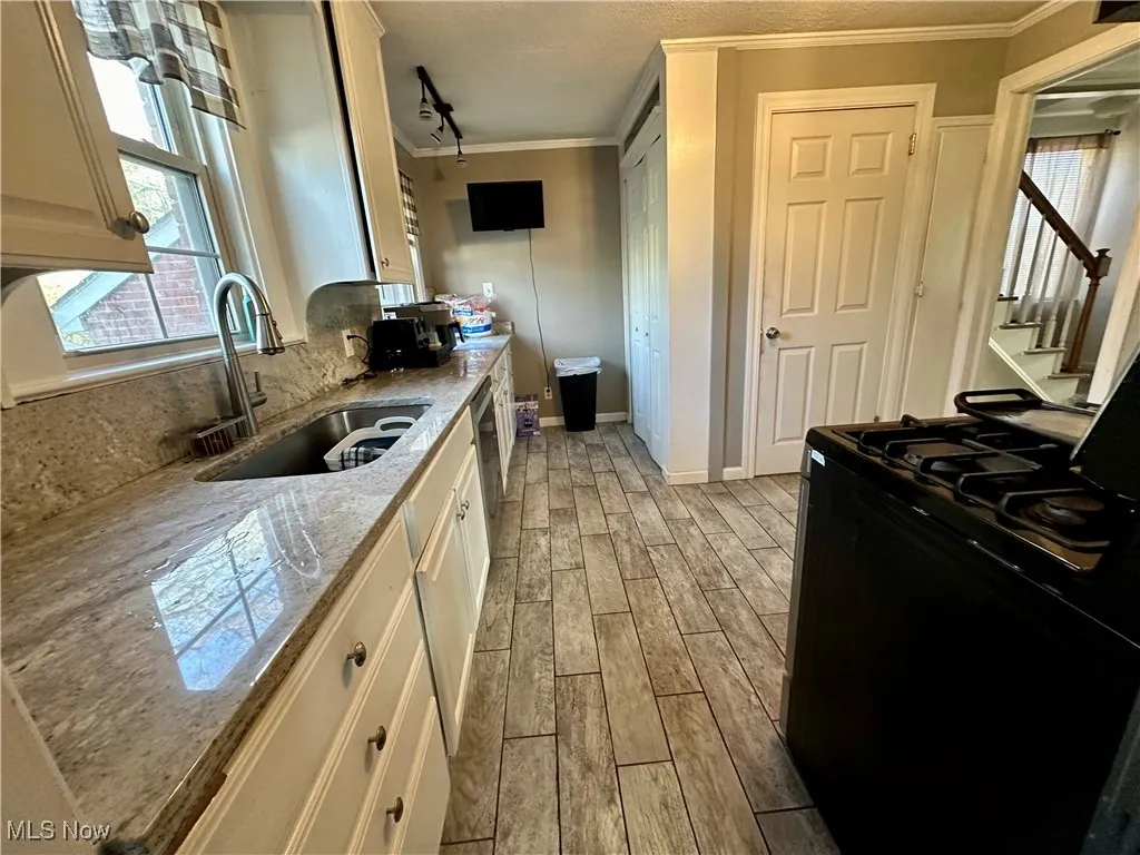 Kitchen with tasteful backsplash, a sink, light wood-style floors, black gas range oven, and ornamental molding