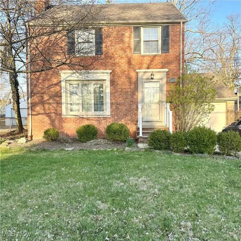 Colonial home with brick siding, a shingled roof, a front lawn, and fence