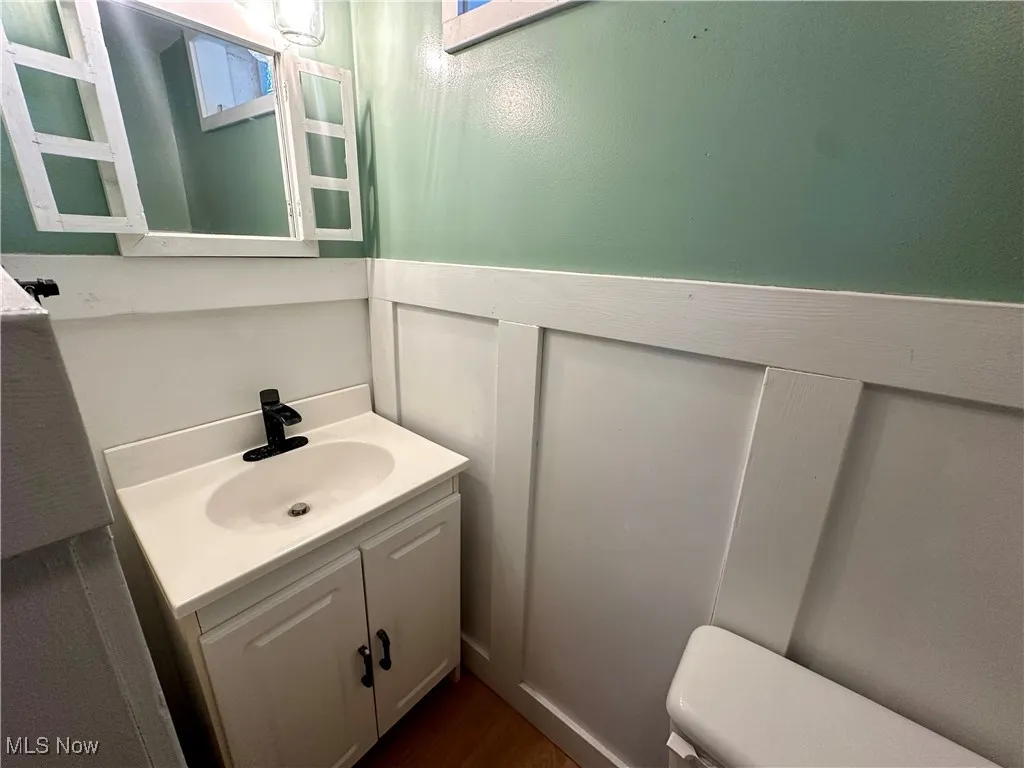 Half bathroom with toilet, wood finished floors, and vanity