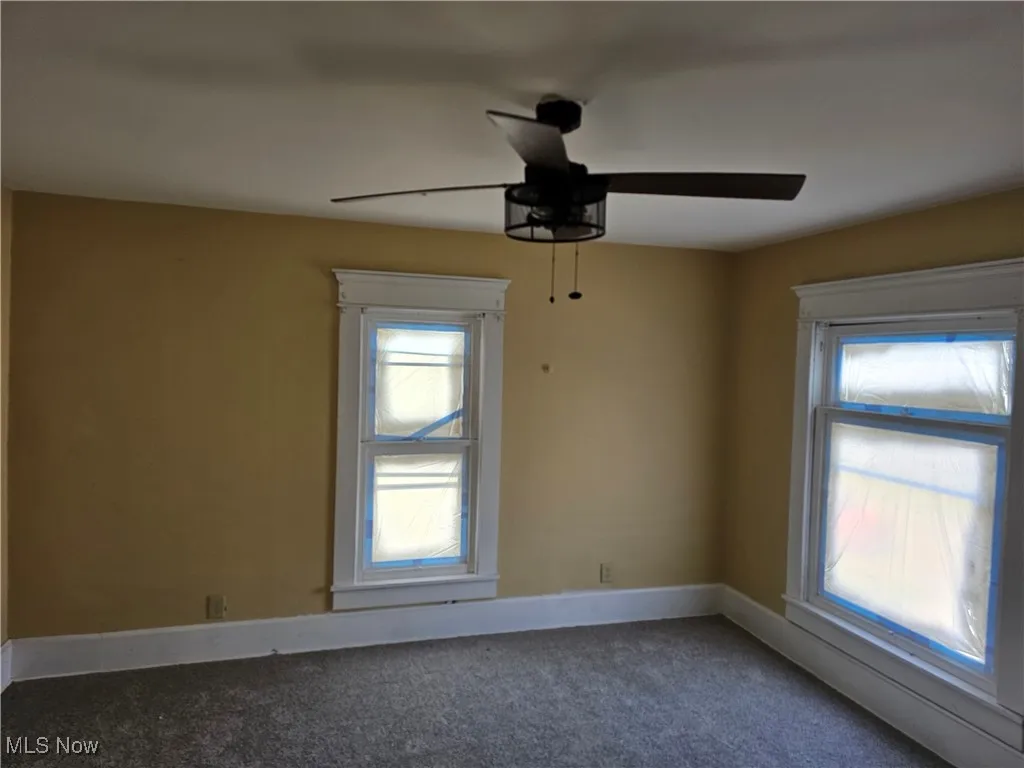 Carpeted spare room featuring plenty of natural light, baseboards, and ceiling fan