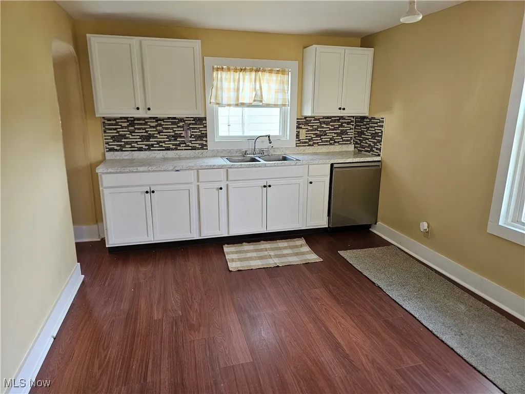 Kitchen with backsplash, stainless steel dishwasher, a sink, baseboards, and white cabinetry