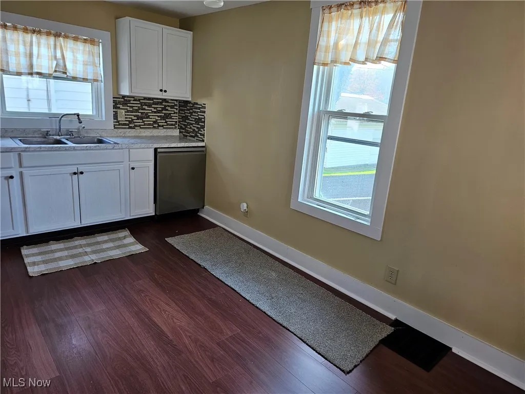 Kitchen with dark wood-style floors, a sink, light countertops, baseboards, and dishwasher
