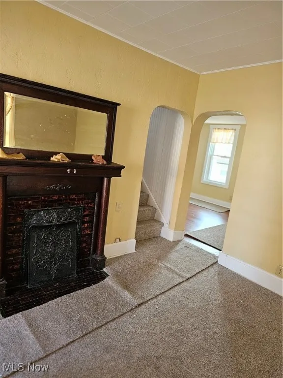 Unfurnished living room with crown molding, a high end fireplace, arched walkways, baseboards, and carpet flooring