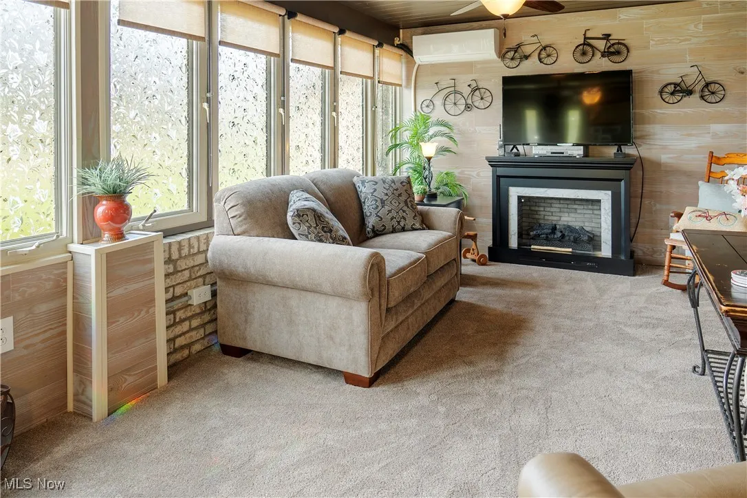 Carpeted living room with a fireplace, an AC wall unit, and a ceiling fan