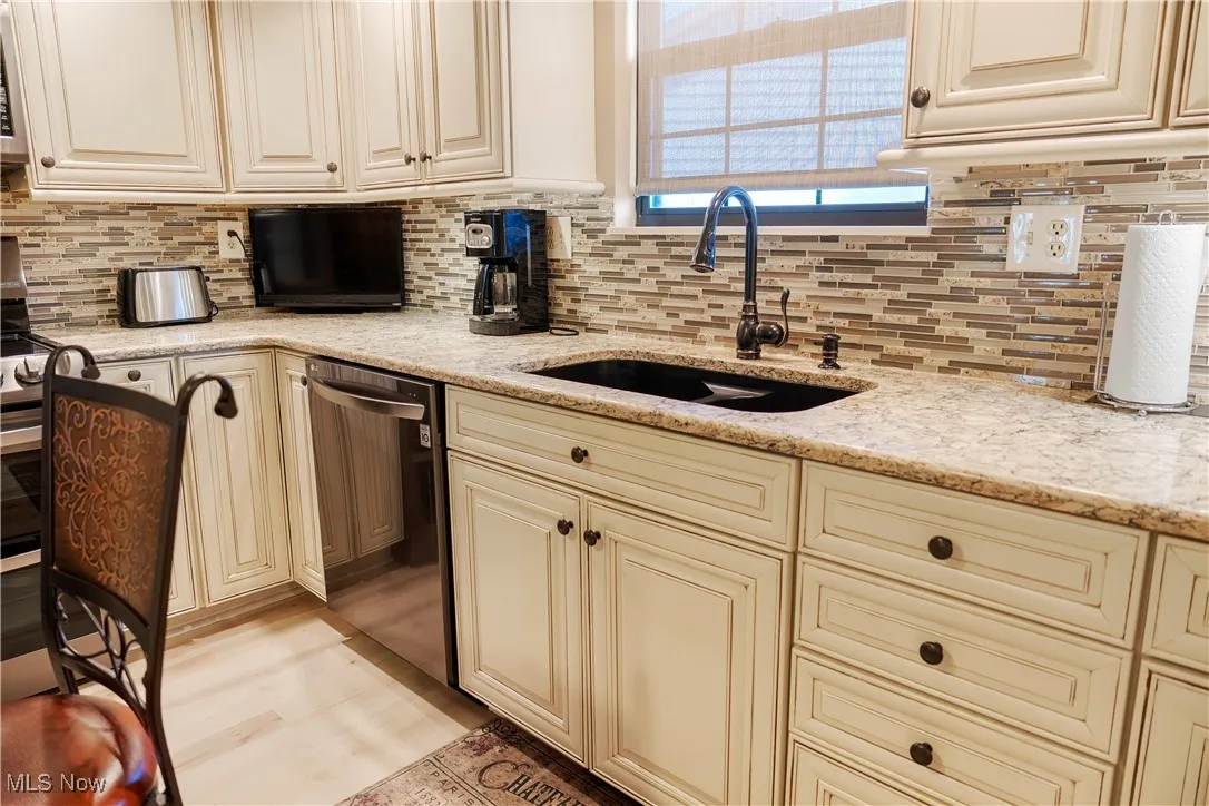 Kitchen featuring backsplash, dishwashing machine, cream cabinetry, and a sink