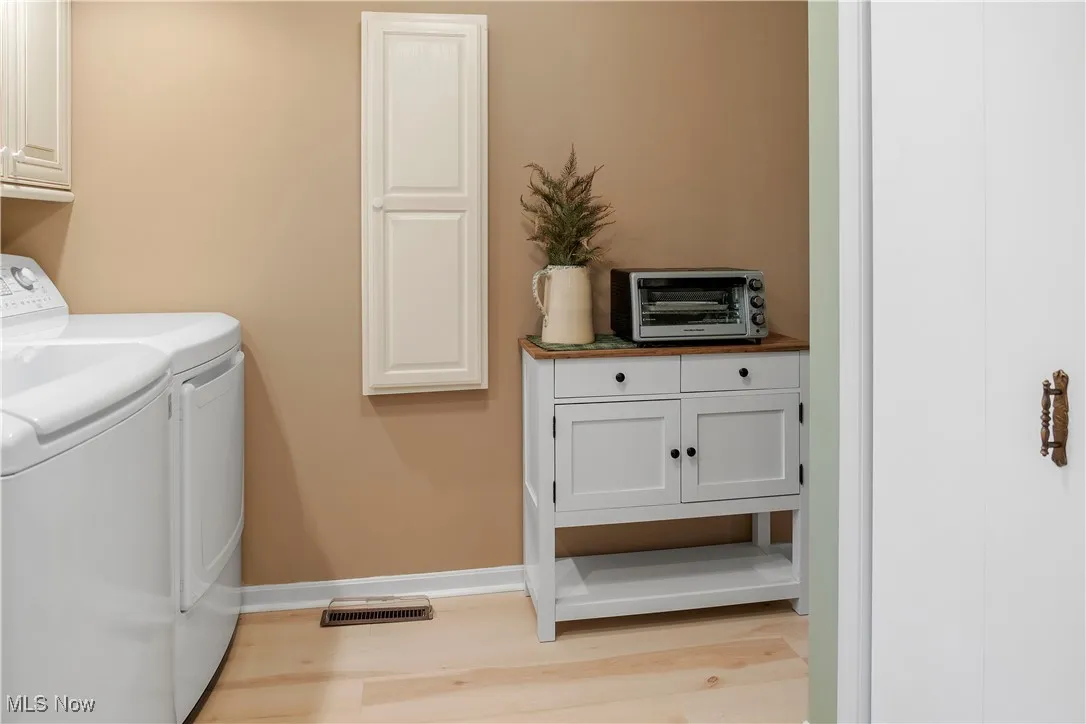 Laundry area with light wood-type flooring, a toaster, washer and clothes dryer, and cabinet space
