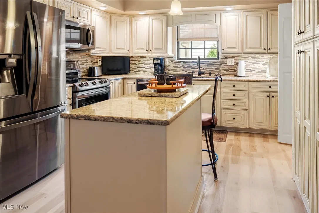 Kitchen with a center island, decorative backsplash, appliances with stainless steel finishes, and light stone countertops