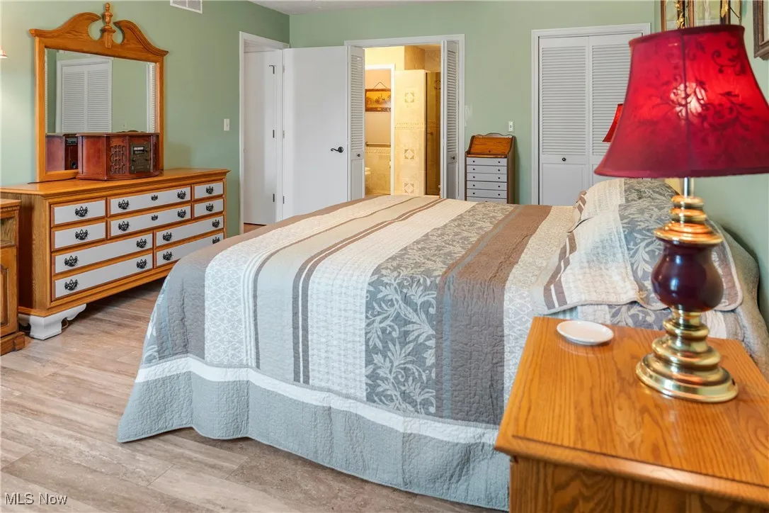 Bedroom with visible vents, ensuite bath, and wood finished floors