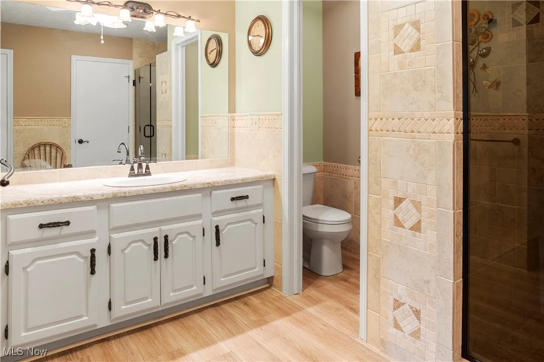 Bathroom featuring a wainscoted wall, wood finished floors, toilet, tile walls, and a stall shower