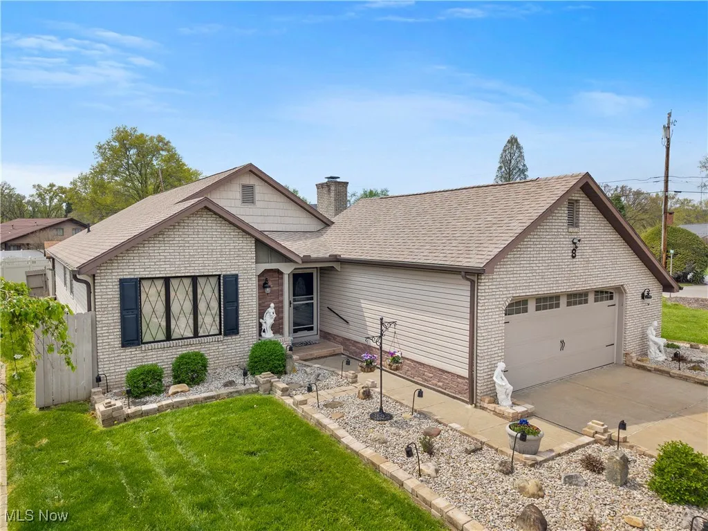 Single story home with roof with shingles, a chimney, brick siding, an attached garage, and a front yard