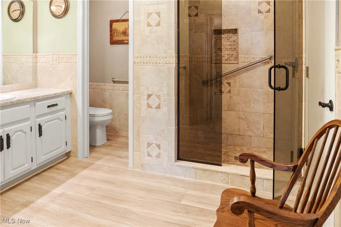 Full bathroom with a shower stall, toilet, vanity, tile walls, and wainscoting