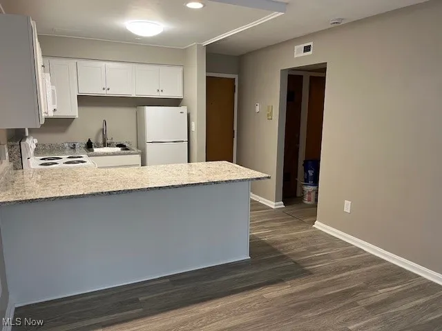Kitchen featuring a peninsula, a sink, dark wood-style flooring, baseboards, and white appliances