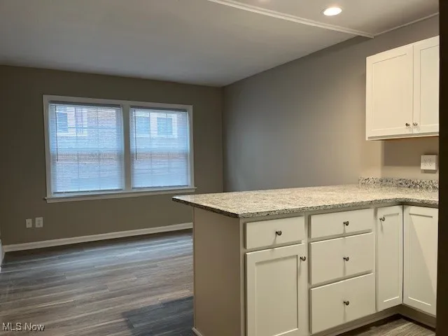 Kitchen featuring white cabinets, a peninsula, baseboards, and dark wood-style flooring