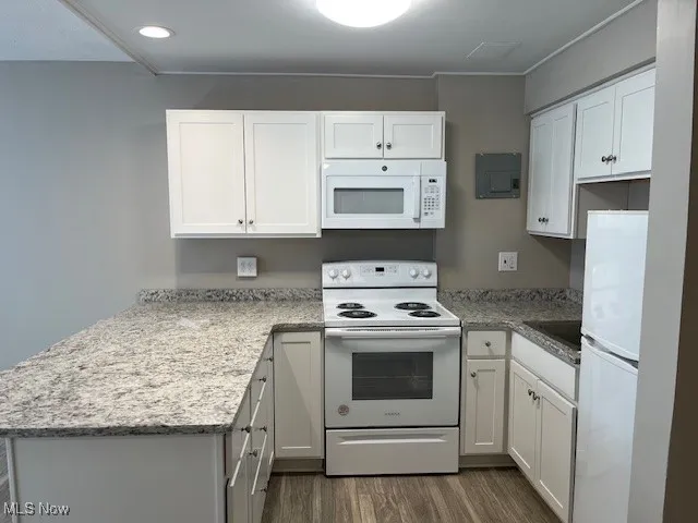 Kitchen with white cabinets, a peninsula, dark wood-type flooring, and white appliances