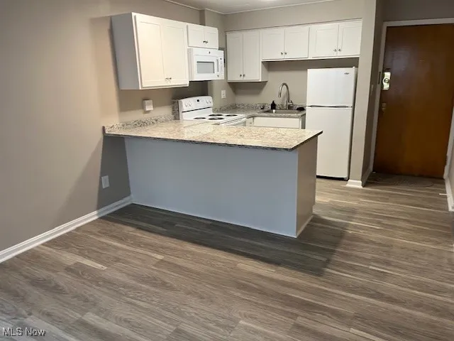 Kitchen featuring a peninsula, dark wood-style flooring, a sink, and white appliances