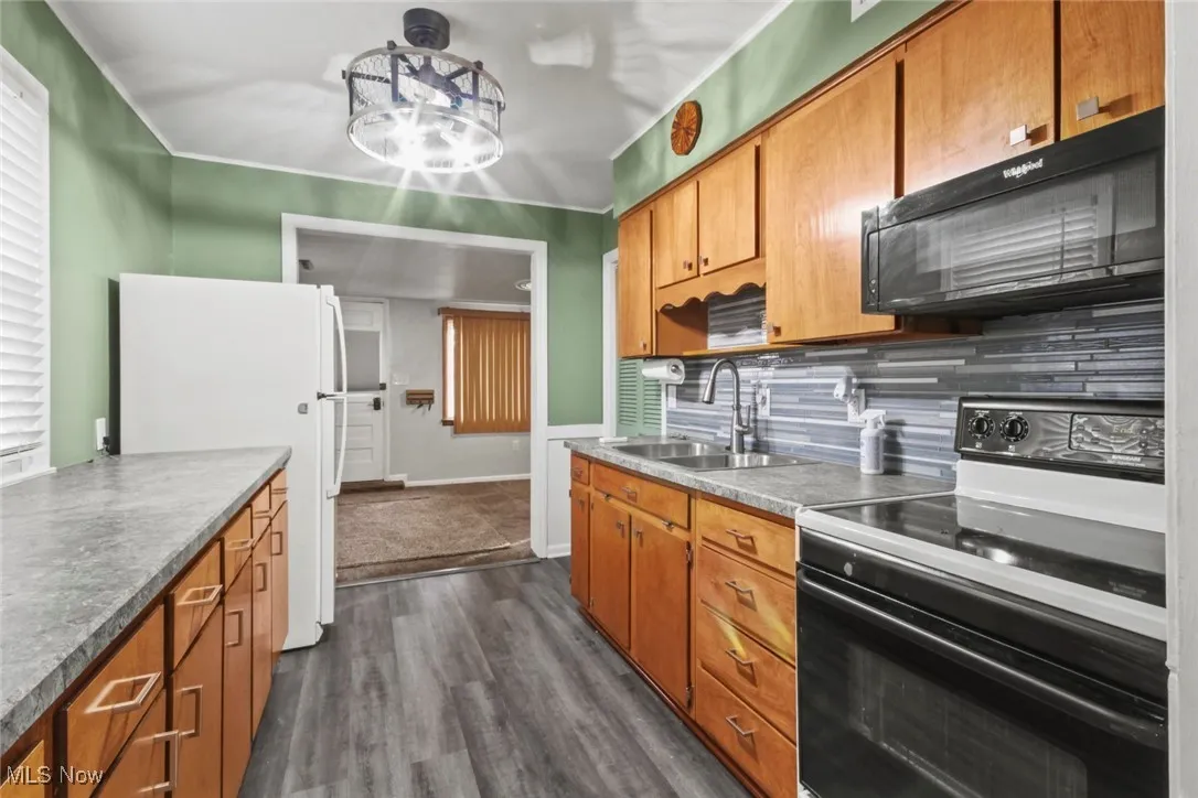 Kitchen featuring black appliances, brown cabinets, dark wood-style floors, decorative backsplash, and crown molding