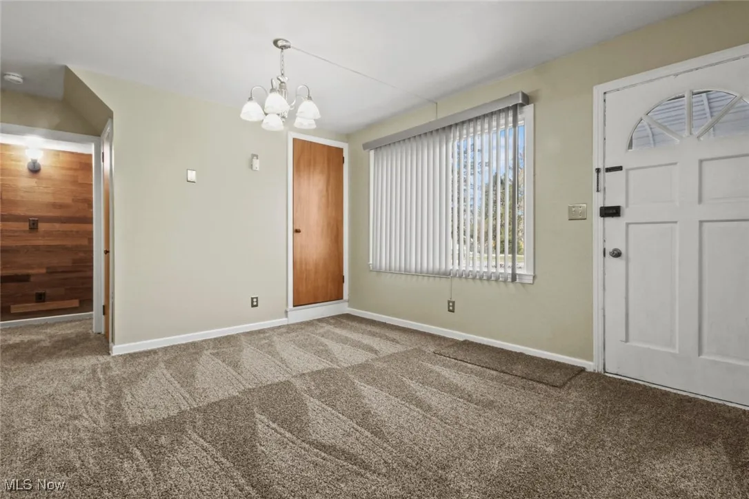 Carpeted foyer featuring a chandelier and baseboards