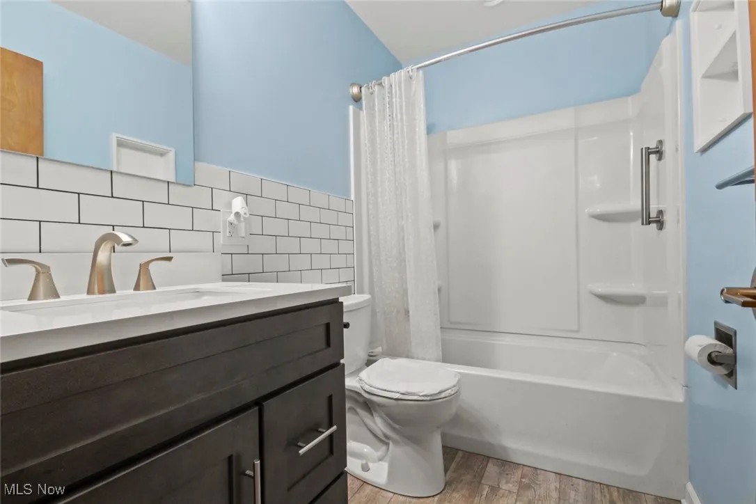 Full bathroom featuring vanity, shower / bath combo with shower curtain, light wood-type flooring, and tile walls