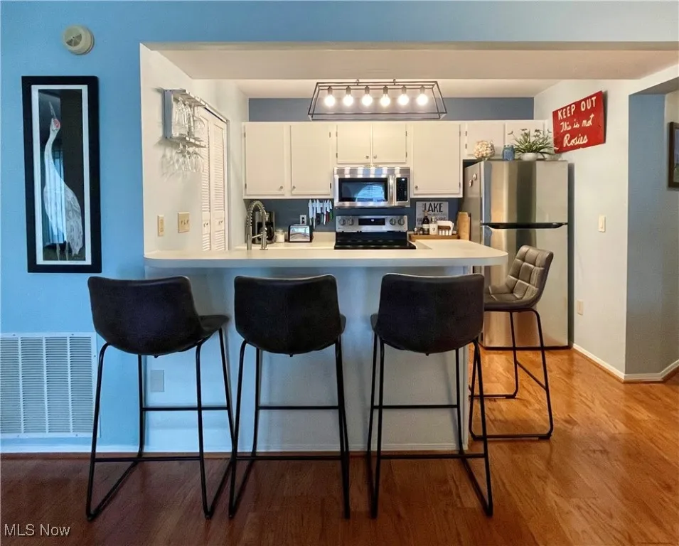 Kitchen featuring visible vents, white cabinetry, appliances with stainless steel finishes, light countertops, and a breakfast bar area