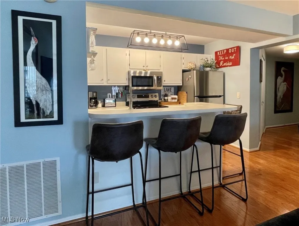 Kitchen featuring white cabinets, stainless steel appliances, visible vents, a peninsula, and a breakfast bar area
