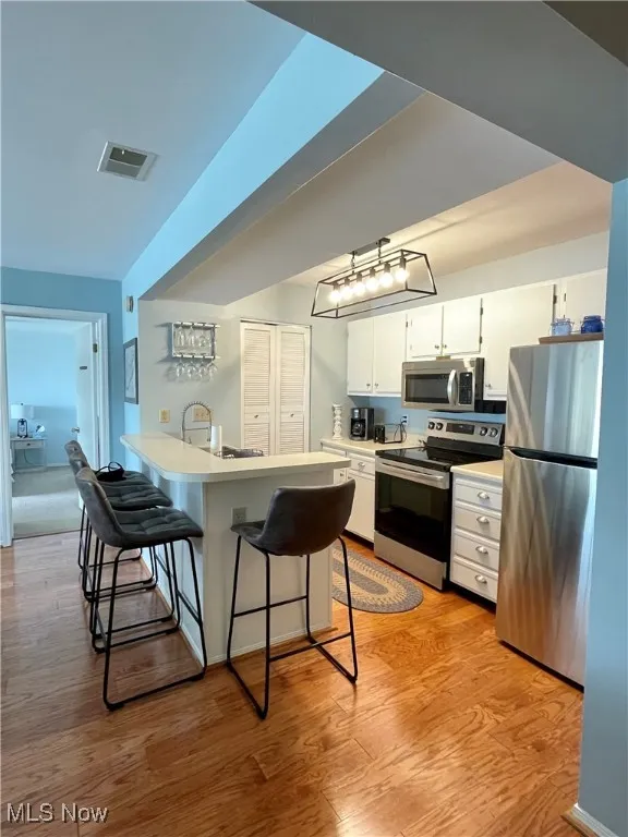 Kitchen featuring white cabinets, a breakfast bar, visible vents, light wood-style flooring, and appliances with stainless steel finishes
