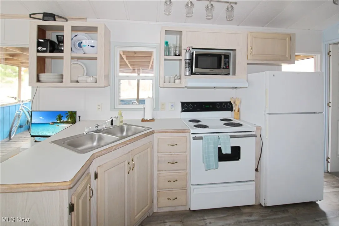 Kitchen with under cabinet range hood, light countertops, white appliances, and a sink