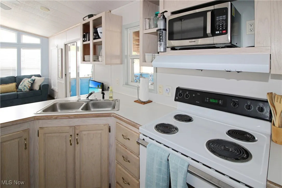 Kitchen with a sink, stainless steel microwave, vaulted ceiling, range with electric stovetop, and light countertops
