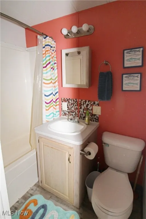 Bathroom with vanity, backsplash, shower / bathtub combination with curtain, and toilet