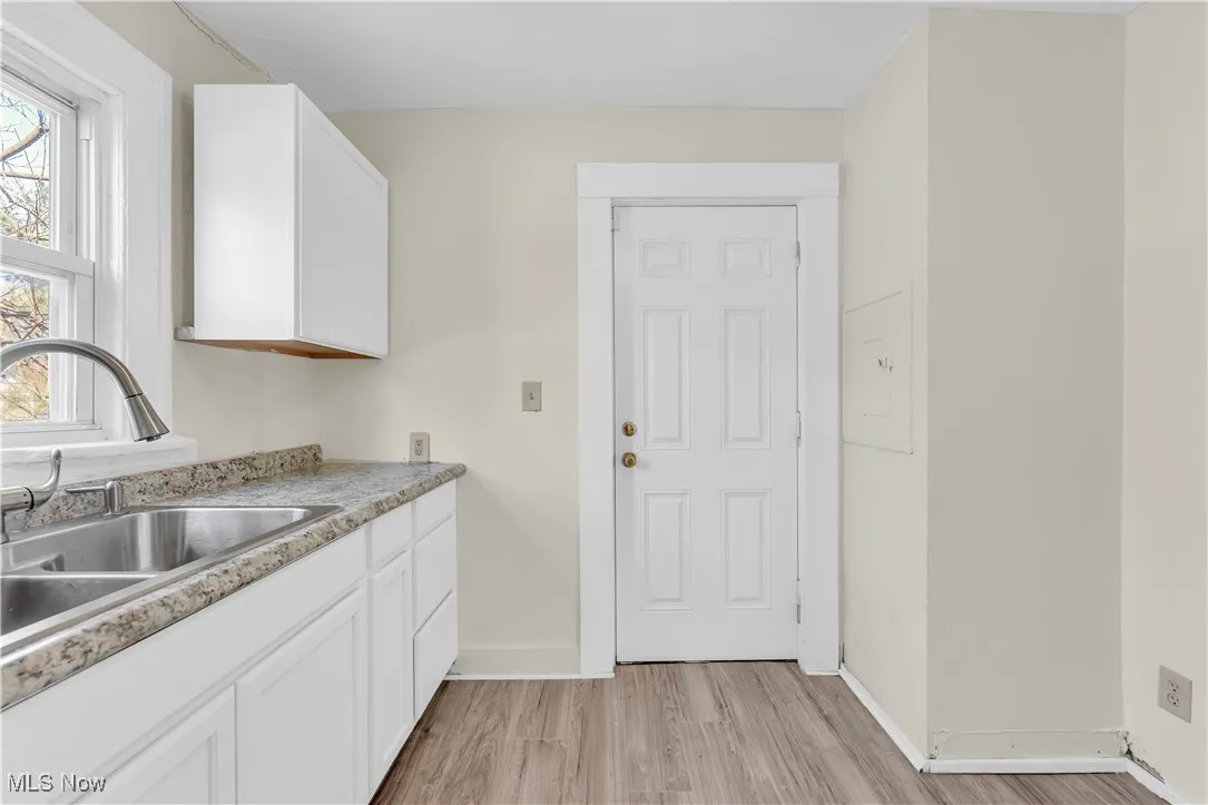 Kitchen with white cabinets, light wood finished floors, light countertops, a sink, and baseboards