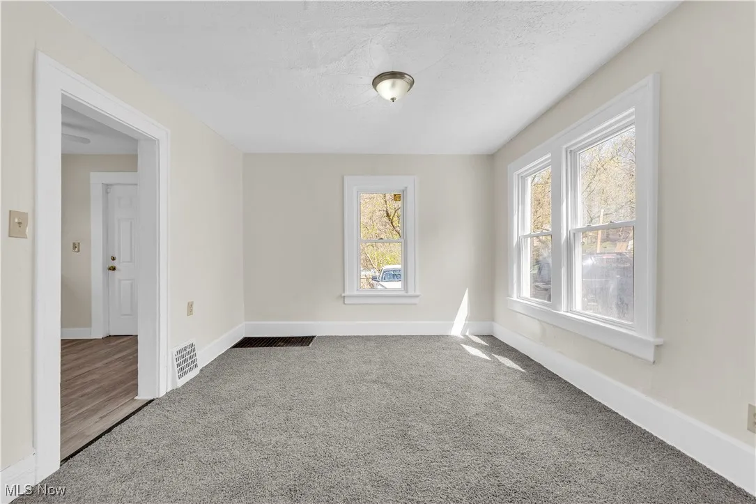 Carpeted spare room with baseboards, a textured ceiling, and visible vents