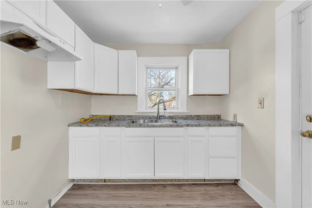 Kitchen with white cabinets, baseboards, under cabinet range hood, and a sink