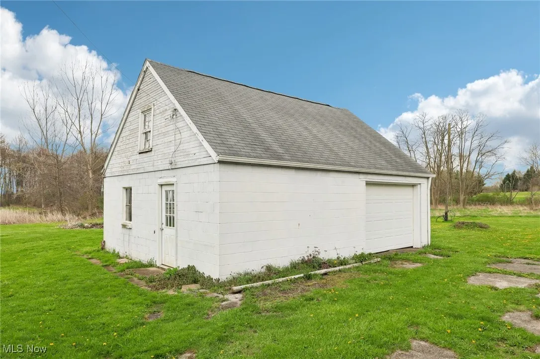 View of property exterior with a detached garage, concrete block siding, an outdoor structure, a yard, and roof with shingles