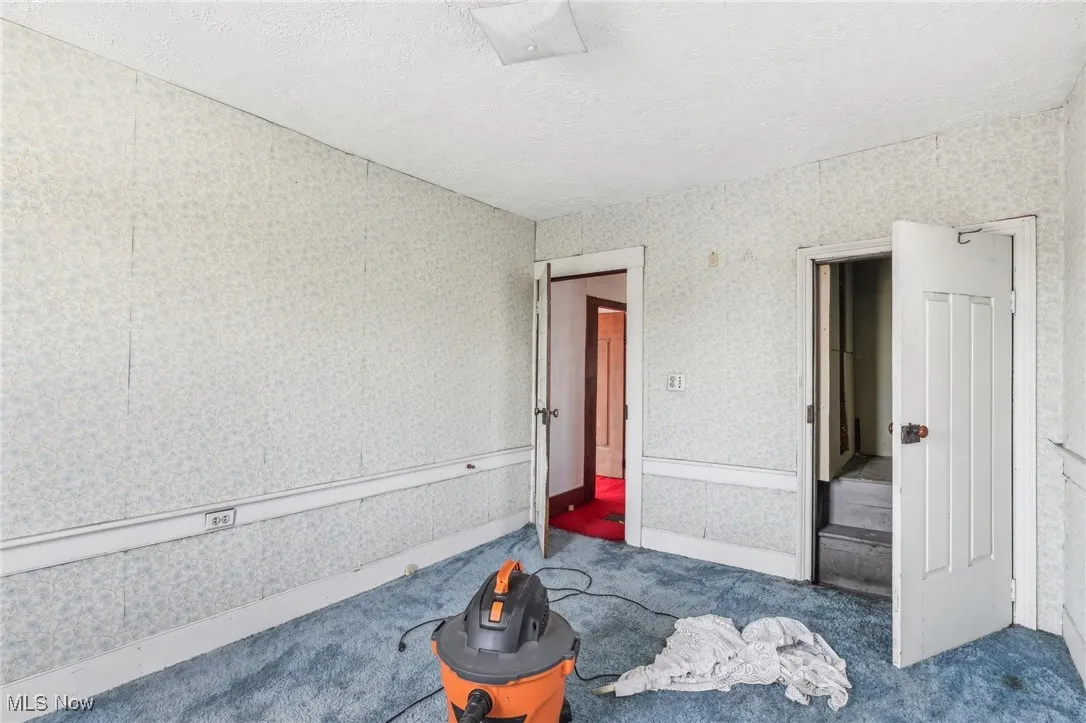 Unfurnished bedroom featuring wallpapered walls, carpet, and a textured ceiling