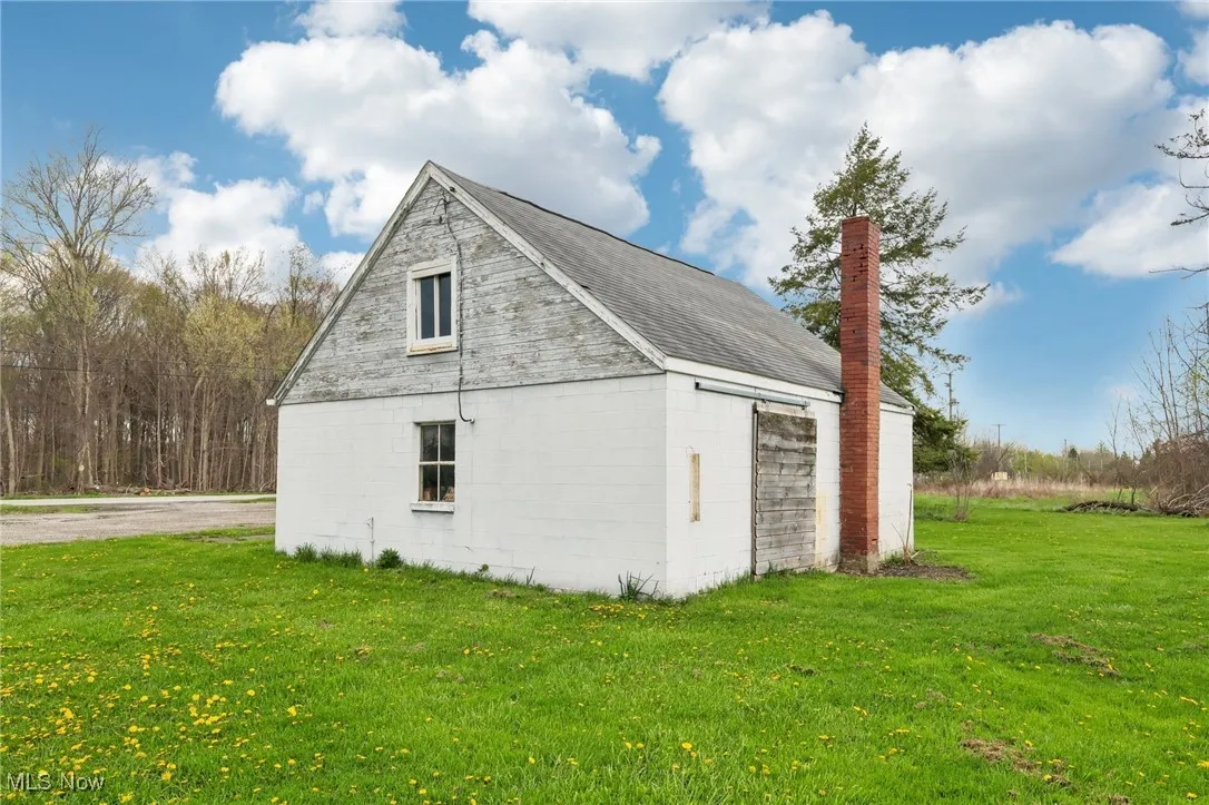 View of property exterior with a chimney, concrete block siding, an outdoor structure, a yard, and a garage