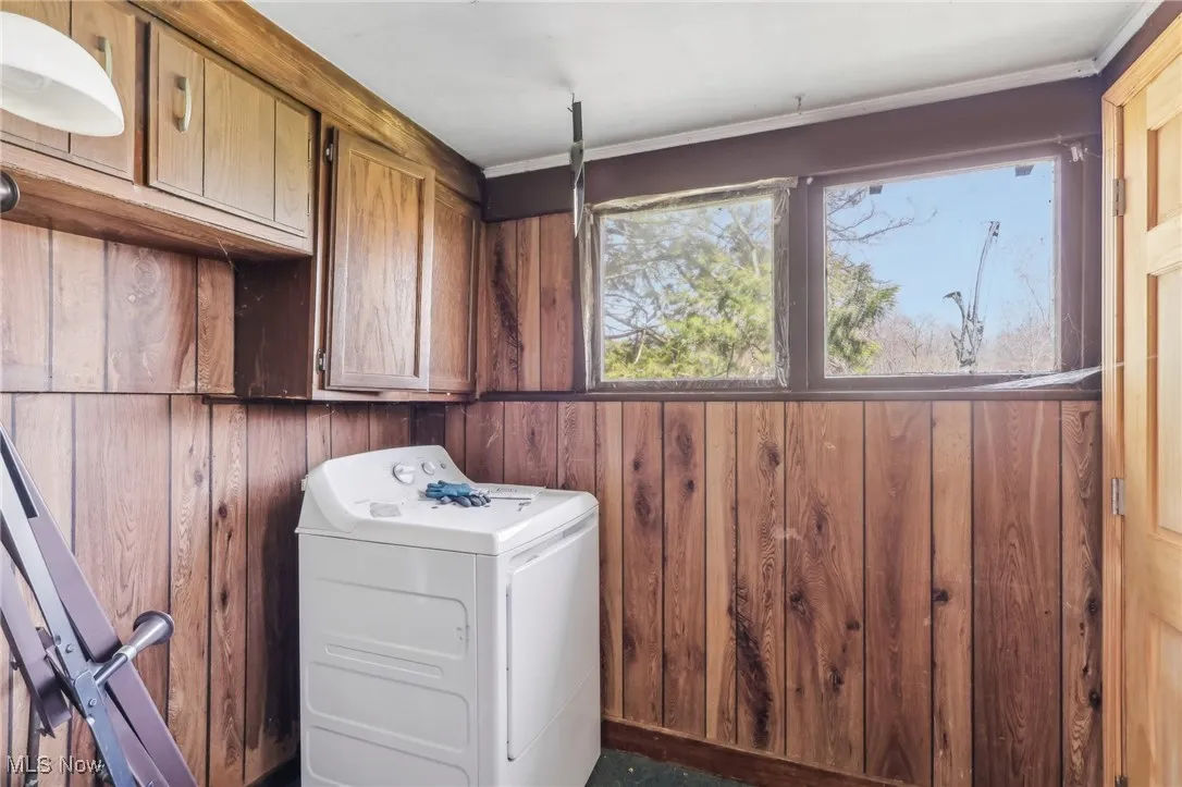 Laundry area with wood walls, washer / clothes dryer, and cabinet space