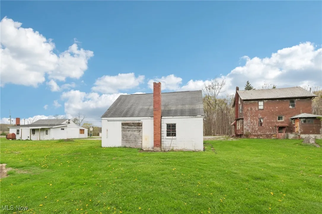 Back of house featuring a chimney, an outdoor structure, a yard, and a barn