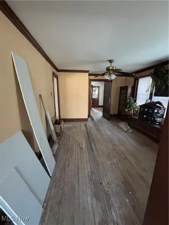 Unfurnished living room with crown molding, baseboards, ceiling fan, and wood-type flooring
