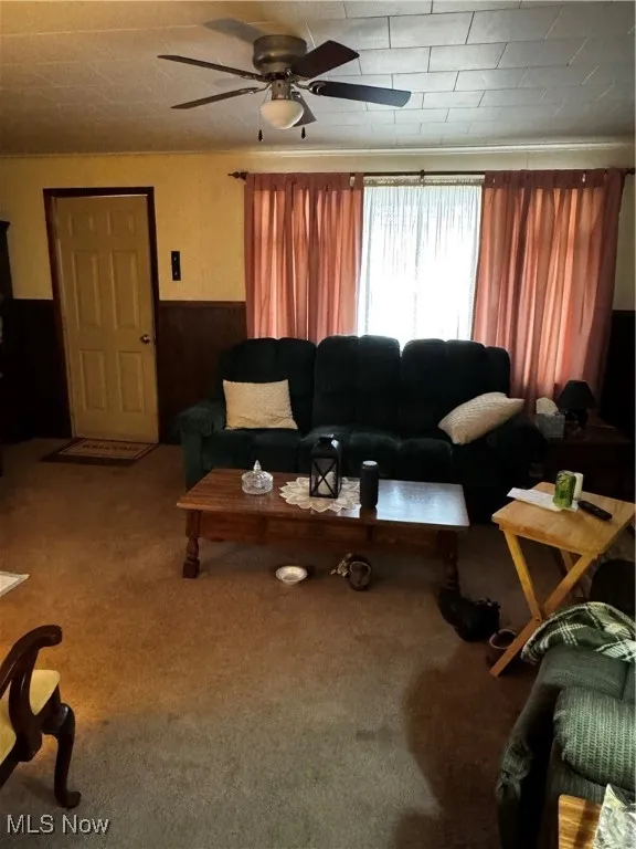 Carpeted living area with ceiling fan and a wainscoted wall