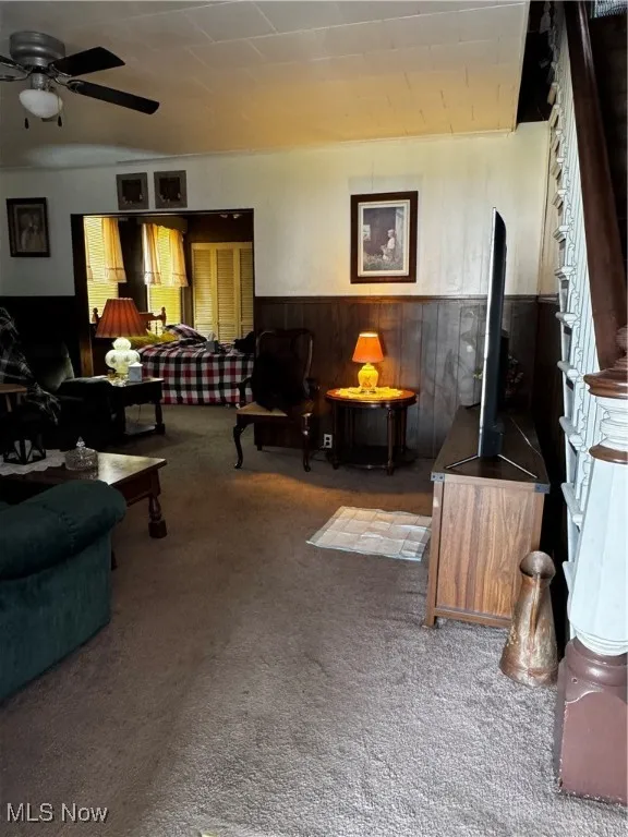 Living area with a wainscoted wall, wood walls, carpet floors, and ceiling fan