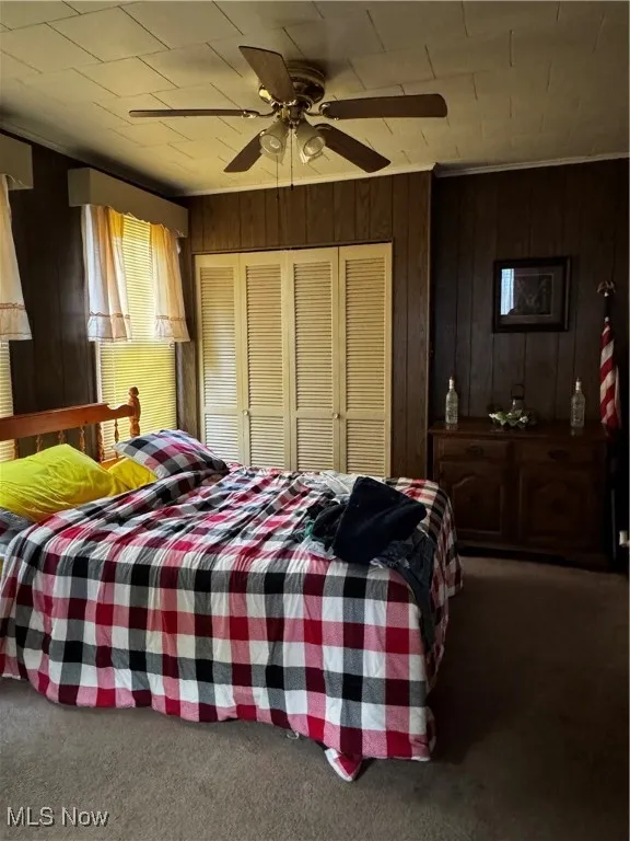 Carpeted bedroom with a ceiling fan, wood walls, and a closet