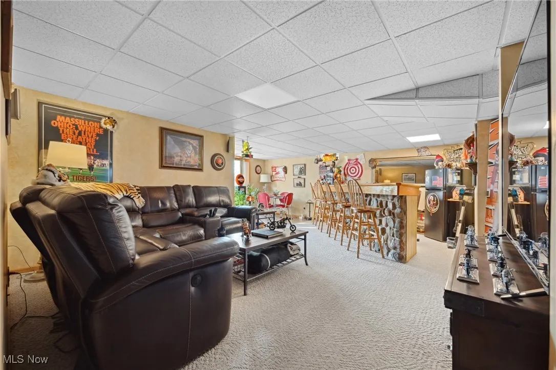 Living area with a dry bar, carpet flooring, and a drop ceiling
