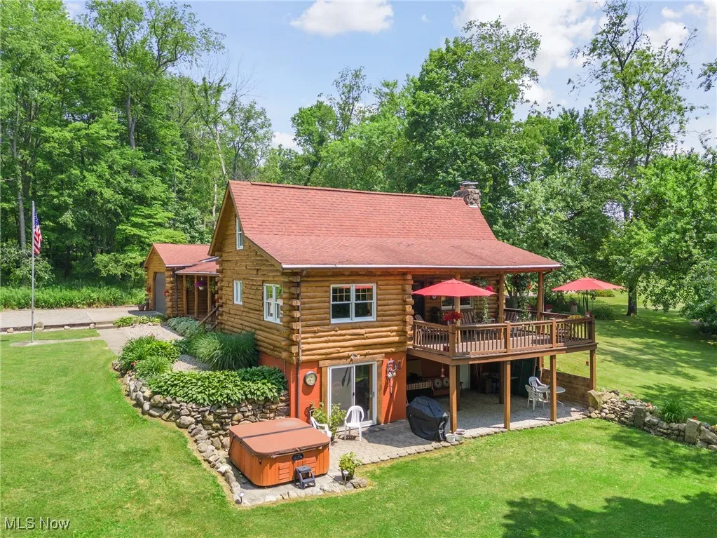 Back of house with a hot tub, a deck, log siding, a lawn, and a chimney