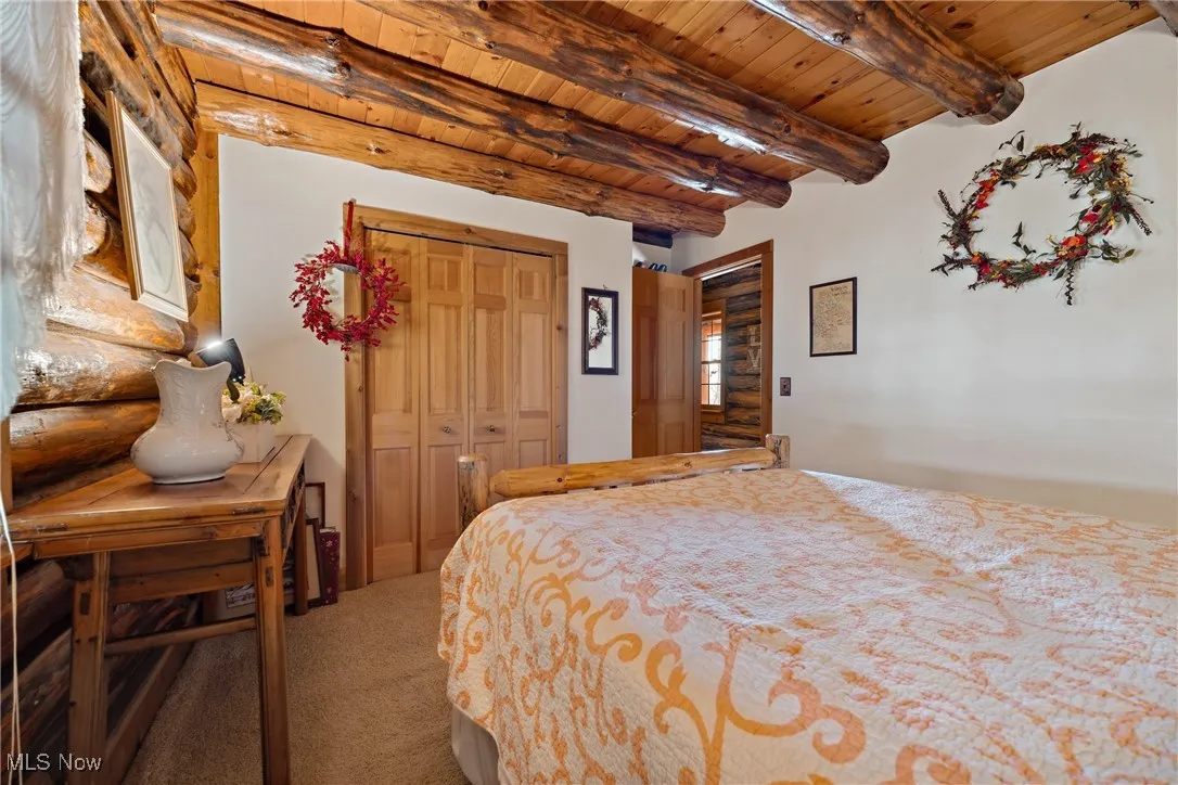 Bedroom with rustic walls, beam ceiling, carpet, and wood ceiling