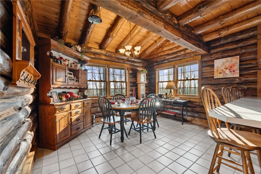 Dining space featuring light tile patterned floors, a chandelier, rustic walls, and wooden ceiling
