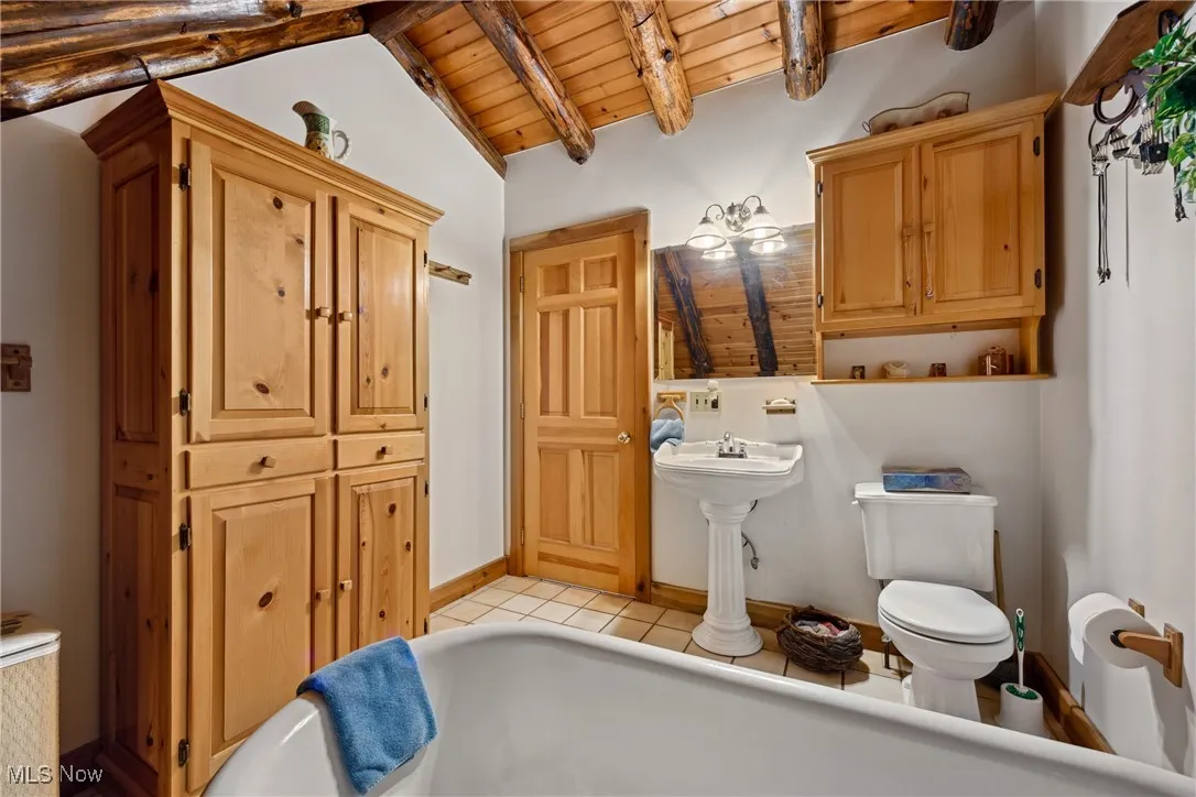 Bathroom featuring toilet, wood ceiling, lofted ceiling with beams, a bath, and tile patterned floors