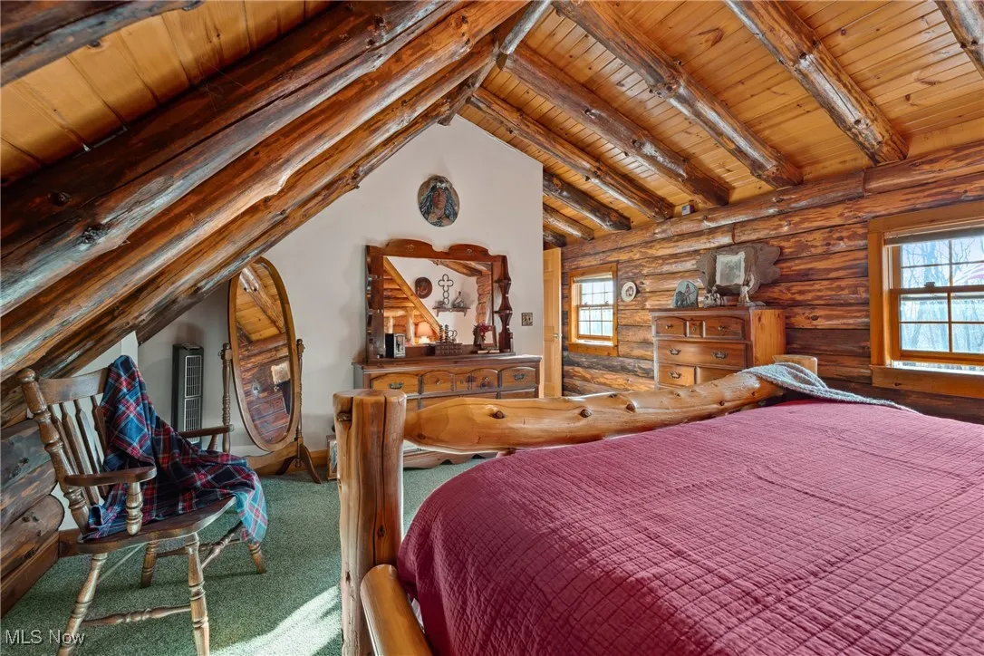 Carpeted bedroom with vaulted ceiling with beams, wood ceiling, and log walls