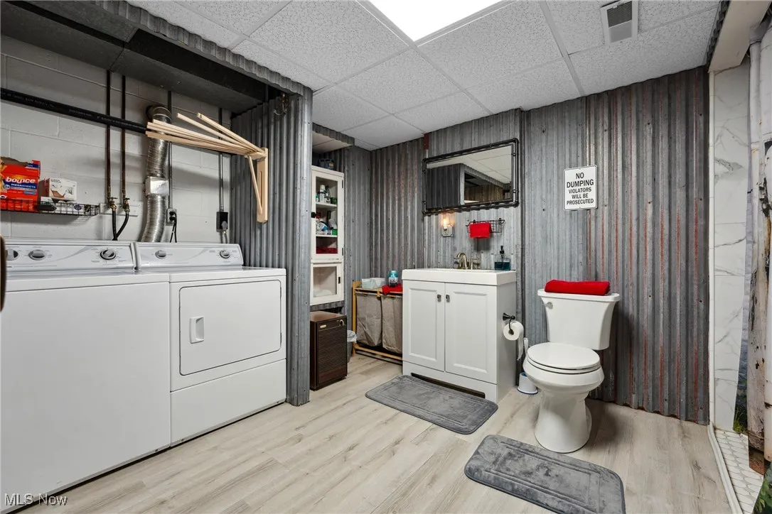 Laundry area with light wood finished floors, visible vents, washer and clothes dryer, laundry area, and a sink
